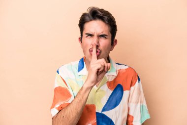 Beyazlı genç bir adam bej arka planda izole edilmiş bir şekilde sır saklıyor ya da sessizlik istiyor..