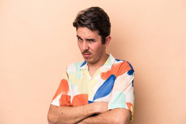 Beyazlı genç bir adam bej arka planda izole edilmiş şüpheli, belirsiz, seni muayene ediyor..