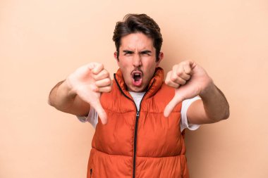 Beyazların arka planında izole edilmiş genç beyaz bir adam baş parmağını aşağı gösteriyor ve hoşlanmadığını ifade ediyor..