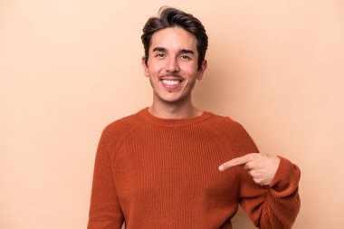 Beyazlı genç bir adam bej arka planda izole edilmiş. Elle bir gömlek fotokopi alanını işaret ediyor. Gururlu ve kendinden emin.