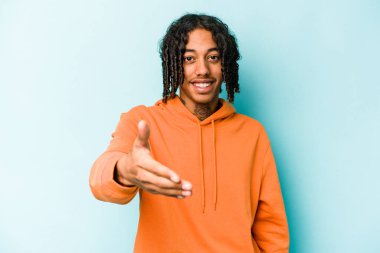 Genç Afro-Amerikan adam mavi arka planda izole edildi. Kameraya doğru elini uzatarak selamlama hareketi yapıyor..