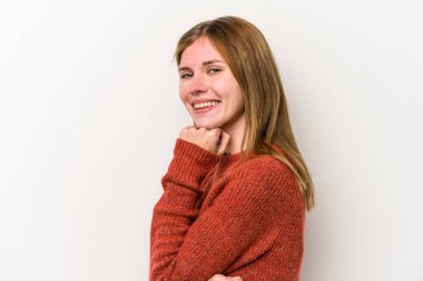 Beyaz arka planda izole edilmiş genç bir Rus kadın mutlu ve kendinden emin gülümsüyor, elleriyle çenesine dokunuyor..