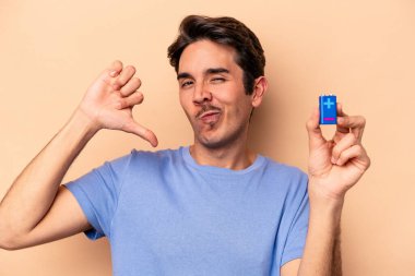 Beyazlı genç bir adam bej arka planda izole edilmiş bir bateriyi tutuyor gururlu ve kendinden emin hissediyor, örnek olarak.