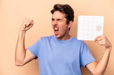 Beyazlı genç bir adam bej arka planda izole edilmiş bir yapboz tutuyor zafer kazandıktan sonra yumruğunu kaldırıyor, kazanan konsept.