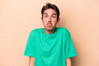 Beyazlı genç adam bej arka planda izole edilmiş omuzlarını silkeliyor ve gözleri açık..