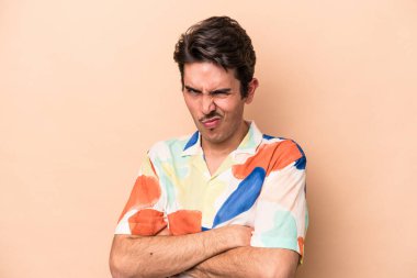 Beyazlı genç bir adam bej arka planda izole edilmiş hoşnutsuzca kaşlarını çatmış, kollarını kavuşturmuş..