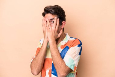 Beyazlı genç bir adam bej arka planda izole edilmiş. Korkmuş ve gergin parmaklarıyla göz kırp..