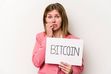 Beyaz arka planda izole edilmiş, tırnak yiyen, gergin ve endişeli bir Bitcoin pankartı tutan genç bir İngiliz iş kadını..