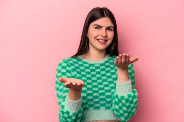 Pembe arka planda izole edilmiş genç beyaz kadın kollarıyla ölçek oluşturuyor, mutlu ve kendinden emin hissediyor..