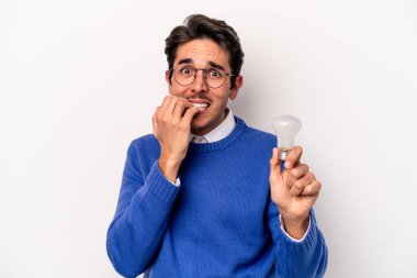 Beyaz arka planda izole edilmiş, tırnak yiyen, gergin ve endişeli bir ampul tutan genç beyaz bir adam..