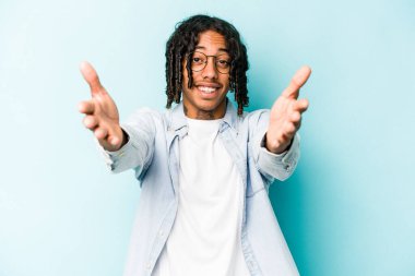 Mavi arka planda izole edilmiş genç Afrikalı Amerikalı adam kameraya sarıldığı için kendinden emin hissediyor..