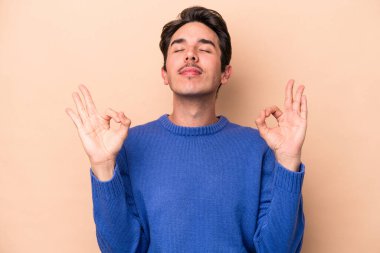 Beyaz tenli genç adam, bej arka planda izole edilmiş yoğun çalışma gününden sonra rahatlıyor, yoga yapıyor..