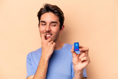 Beyazlı genç bir adam bej arka planda izole edilmiş bir bateriyi tutuyor. Bir şeyin fotokopi alanına baktığını düşünüyor..