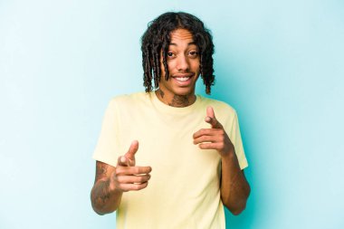 Genç Afrikalı Amerikalı, mavi arka planda izole edilmiş, parmaklarıyla ön tarafı işaret ediyor..