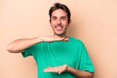 Beyazların arka planında izole edilmiş genç beyaz bir adam iki eliyle bir şey tutuyor, ürün sunumu..