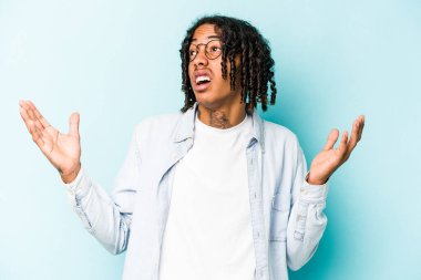 Genç Afrikalı Amerikalı adam mavi arka planda izole edilmiş gökyüzüne haykırıyor, yukarı bakıyor, hayal kırıklığına uğramış..