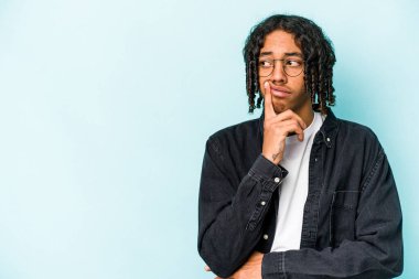 Genç Afrikalı Amerikalı bir adam mavi arka planda izole edilmiş şüpheli ve şüpheci bir ifadeyle yana bakıyor..
