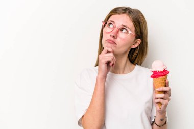 Beyaz arka planda izole edilmiş dondurmayı tutan genç İngiliz kadın şüpheli ve şüpheci bir ifadeyle yana bakıyor..