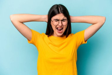 Kafkasyalı genç bir kadın mavi arka planda izole edilmiş kulakları kulaklarıyla kapatıyor çok fazla ses duymamaya çalışıyor..