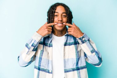 Genç Afrikalı Amerikalı adam mavi arka planda izole edilmiş gülümsüyor, parmaklarını ağıza doğrultuyor..