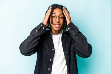 Mavi arka planda izole edilmiş genç Afro-Amerikalı adam mutlu bir şekilde ellerini başının üstünde tutarak gülüyor. Mutluluk kavramı.