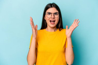 Mavi arka planda izole genç beyaz kadın zaferi ya da başarıyı kutluyor, şaşırıyor ve şok oluyor..