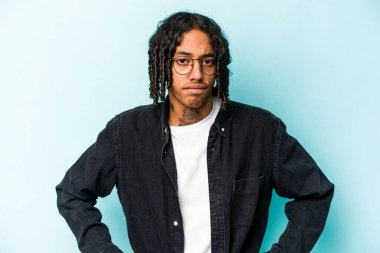 Genç Afrikalı Amerikalı bir adam mavi arka planda izole edilmiş, kafası karışmış, şüpheli ve güvensiz hissediyor..