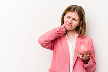 Genç İngiliz kadın elinde bir kumbara tutuyor beyaz arka planda izole edilmiş kafasının arkasına dokunuyor, düşünüyor ve bir seçim yapıyor..