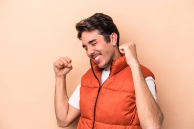 Beyazlı genç adam bej arka planda izole edilmiş özel bir günü kutluyor, atlıyor ve enerjiyle kollarını kaldırıyor..