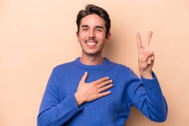 Beyaz tenli genç adam bej arka planda izole edilmiş yemin ediyor, elini göğsüne koyuyor..