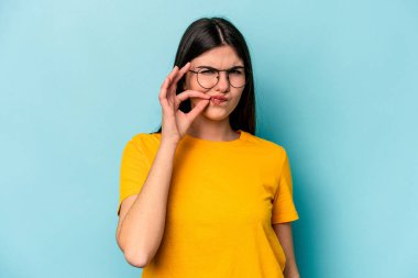 Mavi arka planda izole edilmiş genç beyaz kadın parmakları dudaklarında bir sır saklıyor..