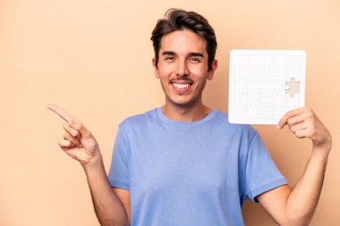 Elinde bej arka planda izole edilmiş bir yapboz tutan genç, beyaz bir adam gülümseyip, boş bir alanda bir şey gösteriyor..