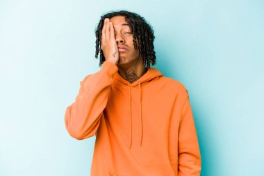 Genç Afrikalı Amerikalı adam mavi arka planda izole edilmiş. Yorgun ve uykulu. Elini başının üstünde tutuyor..