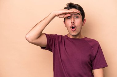 Beyazlı genç bir adam bej arka planda izole edilmiş, uzaklara bakıyor ve elini alnına koyuyor..