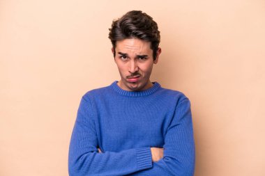 Beyazlı genç adam bej arka planda izole edilmiş. Mutsuz, iğneleyici bir ifadeyle kameraya bakıyor..