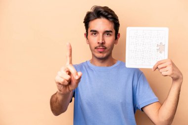Beyazların elinde bir yapboz tutan genç bir adam bej arka planda bir numarayı parmağıyla gösteriyor..