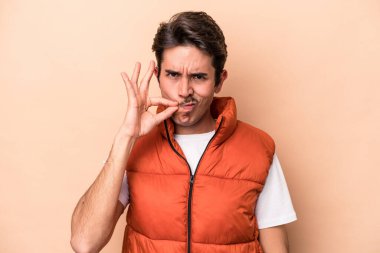 Beyazlı genç bir adam bej arka planda izole edilmiş ve parmakları dudaklarında bir sır saklıyor..
