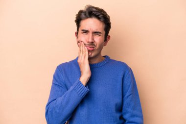 Beyazlı genç bir adam bej arka planda izole edilmiş güçlü bir diş ağrısı ve azı dişi ağrısı var..