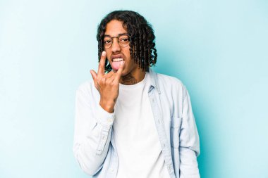 Genç Afrikalı Amerikalı adam mavi arka planda izole edilmiş. Parmaklarıyla kaya hareketi gösteriyor.