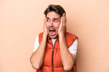 Beyazlı genç bir adam bej arka planda izole edilmiş kulakları kulaklarıyla kapatıyor çok fazla ses duymamaya çalışıyor..