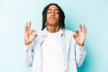 Genç Afrikalı Amerikalı erkek mavi arka planda izole edilmiş yoğun bir günün ardından rahatlıyor, yoga yapıyor..