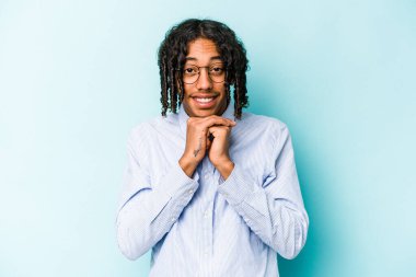 Mavi arka planda izole edilmiş genç Afrikalı Amerikalı ellerini çenesinin altında tutuyor ve mutlu bir şekilde yan tarafa bakıyor..