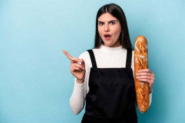 Genç fırıncı Kafkas elinde bir somun ekmek var. Mavi arka planda izole edilmiş. Yan tarafı işaret ediyor.