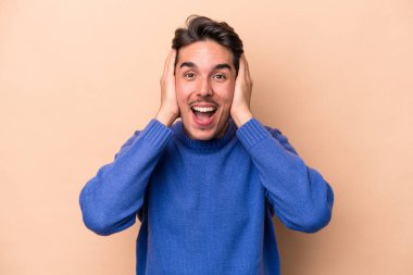 Beyaz tenli genç adam bej arka planda izole edilmiş bağırıyor, çok heyecanlı, tutkulu, bir şeyden memnun..