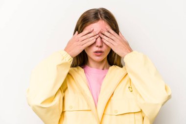 Beyaz arka planda soyutlanmış genç bir İngiliz kadın elleriyle gözlerini kapatmaktan korkuyor..