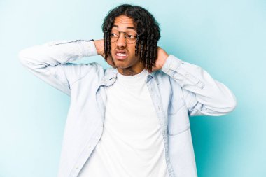 Genç Afrikalı Amerikalı bir adam mavi arka planda izole edilmiş. Oturaklı yaşam tarzından dolayı boyun ağrısı çekiyor..