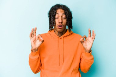 Genç Afrikalı Amerikalı erkek mavi arka planda izole edilmiş yoğun bir günün ardından rahatlıyor, yoga yapıyor..