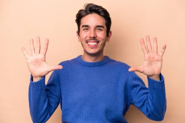 Beyazlı genç adam bej arka planda izole edilmiş. Elleriyle on numarayı gösteriyor..