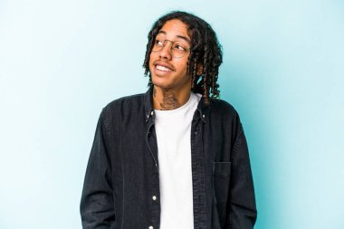 Genç Afrikalı Amerikalı adam mavi arka planda izole edilmiş rahat ve mutlu bir şekilde gülüyor, boynunda dişlerini gösteriyor..