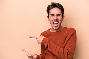 Beyaz tenli genç adam bej arka planda izole edilmiş ve işaret parmağıyla fotokopi alanını işaret ederek heyecan ve arzusunu ifade ediyor..